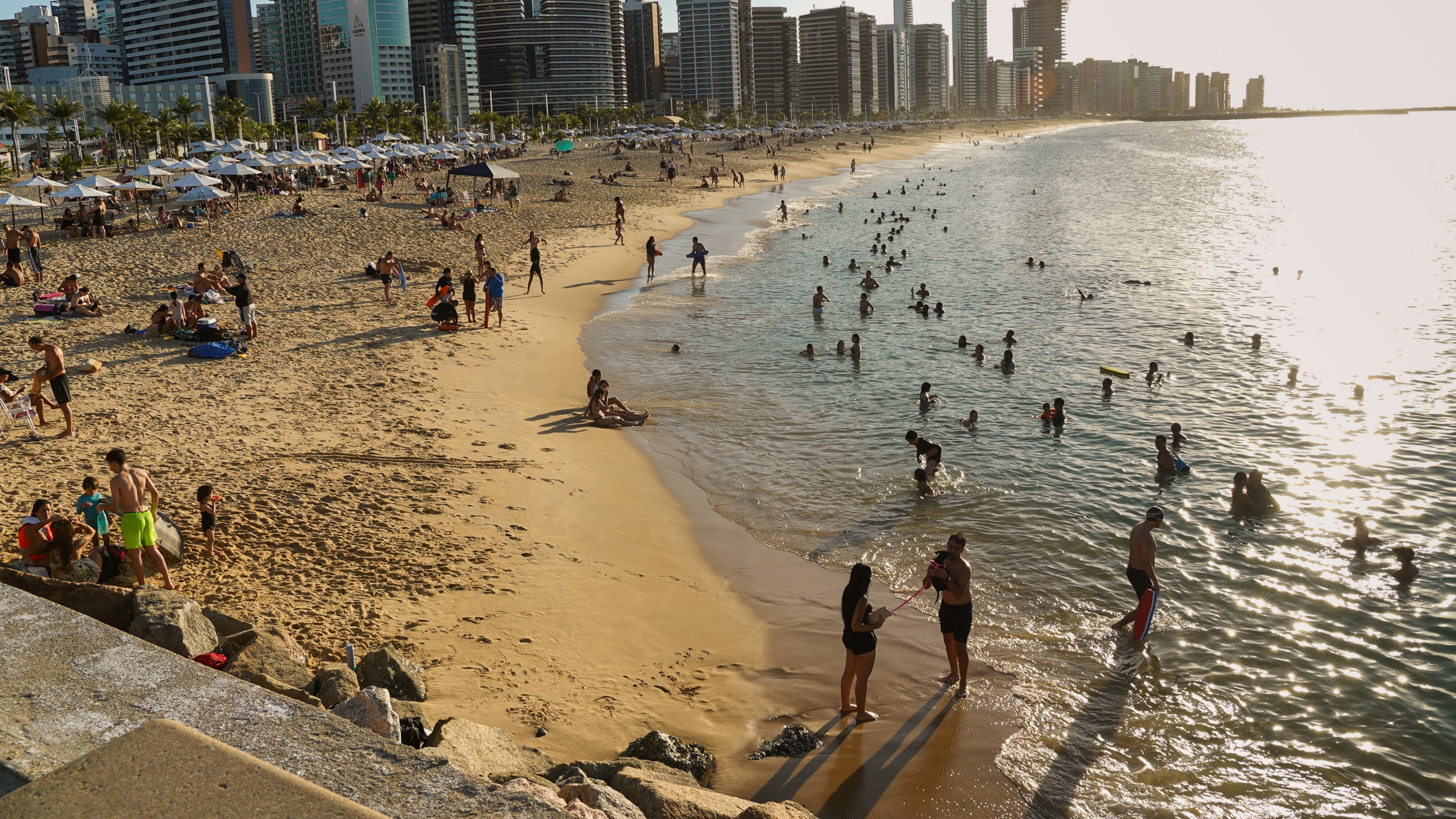 a foto mostra a faixa de areia de uma praia com banhistas